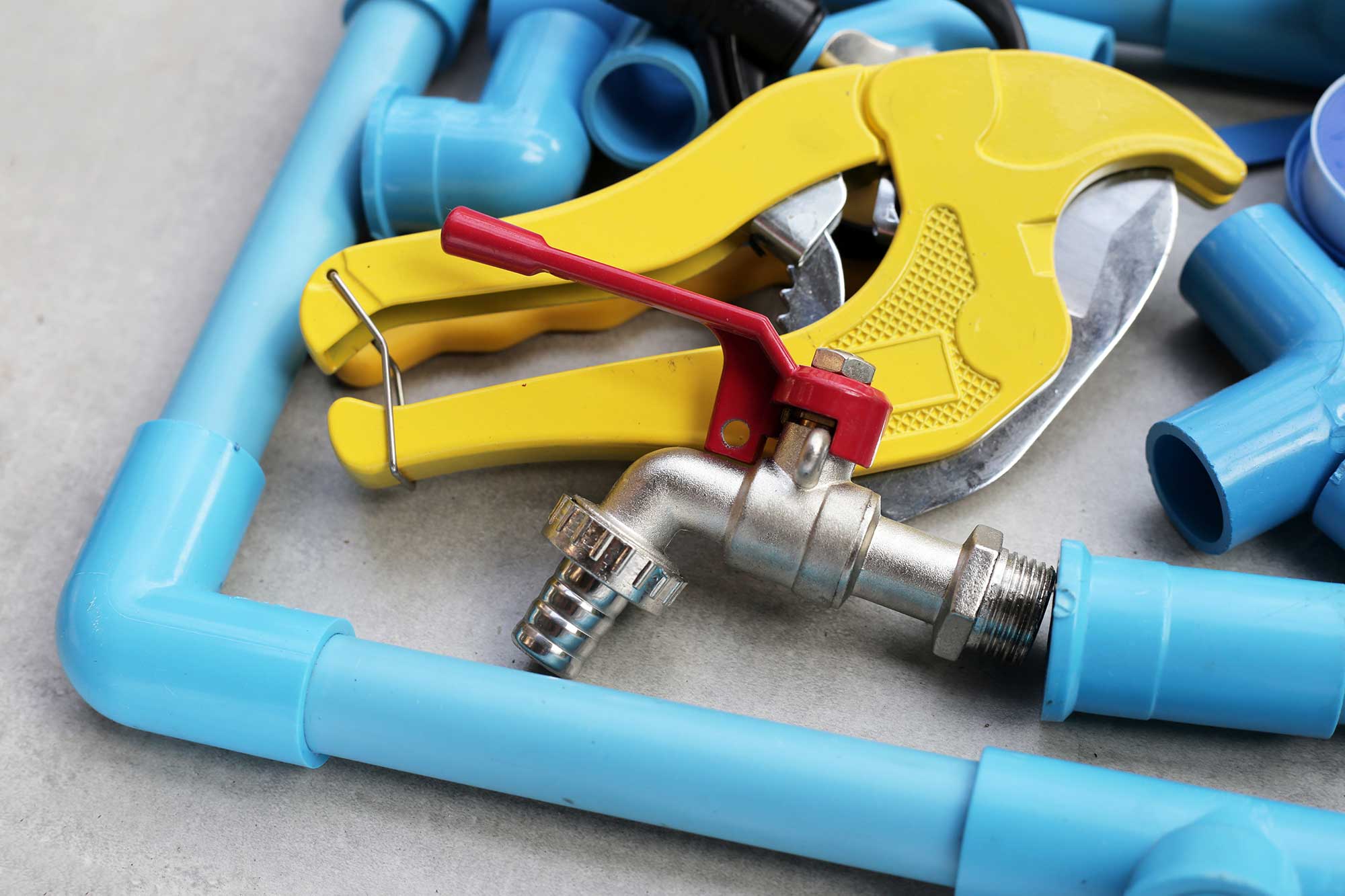 A collection of blue PVC pipes and a yellow pipe cutter, along with a metal valve, arranged on a surface. The tools and materials are used for plumbing repairs.
